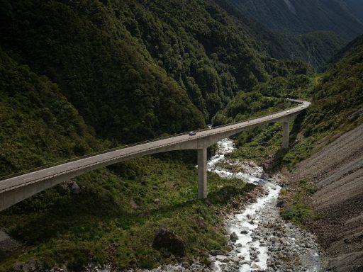 A highway bridge spans a lush green valley with a winding river below.