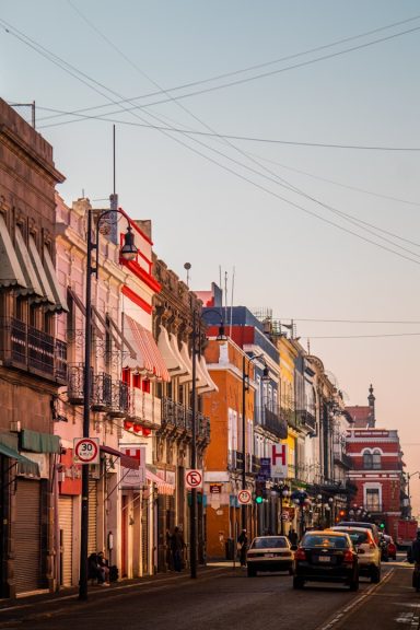 Puebla Colorful buildings line a street at sunset, with parked cars and overhead wires.