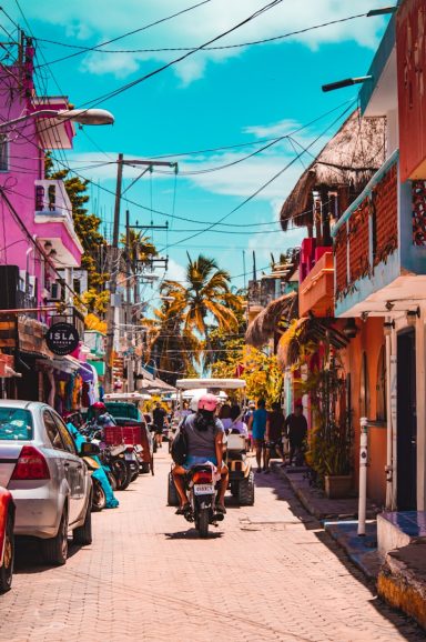 Isla Mujeres Colorful street scene with shops, palm trees, and parked cars under a blue sky.