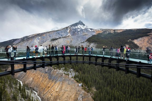 Visitors on a glass bridge overlooking a mountain landscape with dark clouds above.