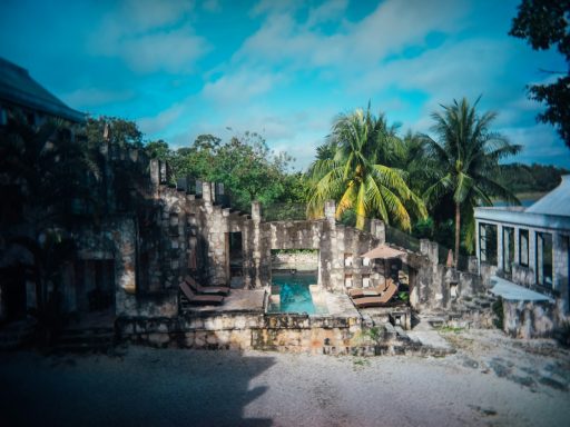 Coba Ruins of a stone building with a swimming pool, surrounded by palm trees under a blue sky.