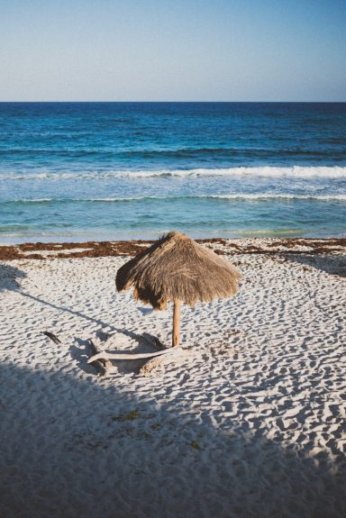 Cozumel Straw umbrella on sandy beach with gentle waves in the background.