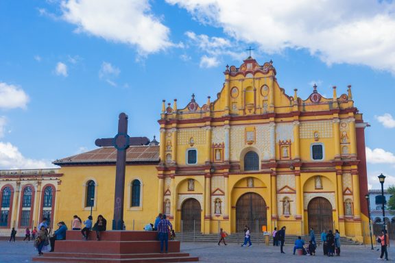 San Cristobal de las Casas Colorful colonial church in a bustling town square, with a large cross in the foreground.
