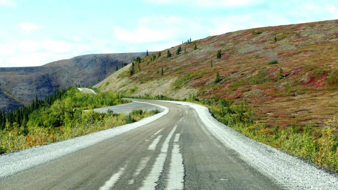 Winding road through a scenic landscape of green hills and distant mountains.