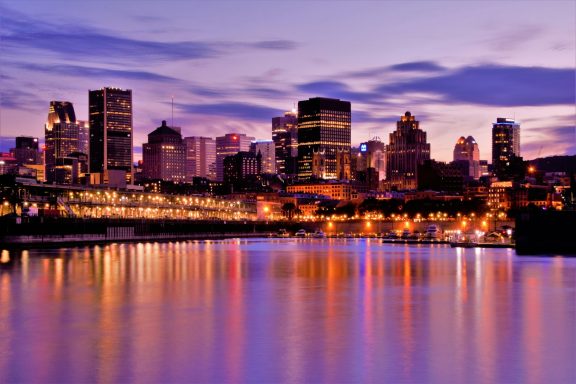 City skyline at dusk reflected in calm water, showcasing vibrant colors and lights.