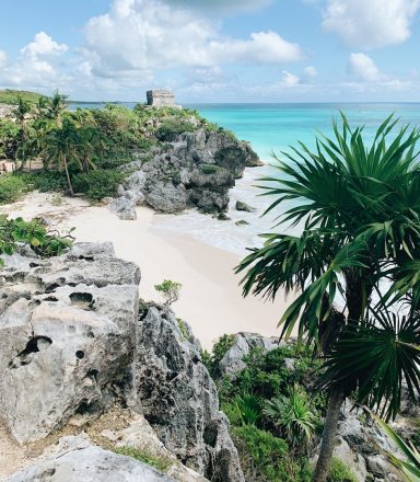 Tulum Tropical beach with rocky cliffs, turquoise water, and lush greenery in Tulum, Mexico.